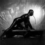 Man in rubber suit on all fours on wooden bench.