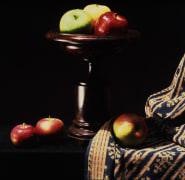 Apples and an urn on a black table draped with a paisley cloth.