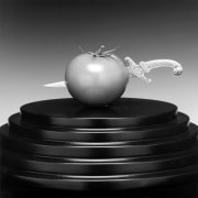 A tomato on a leveled round black stand with a silver dagger pieced though its center.