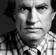Closeup of a man with a serious expression looking into the camera and wearing a checked shirt.