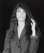 Portrait of a woman in a pinstripe suit with one hand touching her long dark hair.