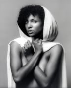 Nude woman from the waist up holding a white piece of fabric around her like a hooded cape.