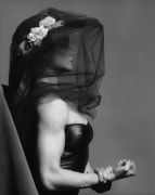 Lisa Lyon in profile wearing a black veil and leather corset, one hand grasping the other arm's wrist.