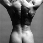 Back view of muscular woman's back and buttocks, with her arms raised upward and back muscles flexed, cropped at the neck and hips.