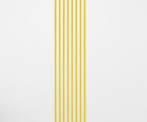 An installation of white gummed paper tape, 8 strips, floor to ceiling, that have a strand of yellow ribbon within each strip.