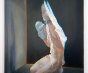 A ghostly woman kneeling on a black ground with a white mask in her hand