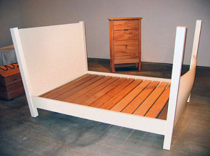 An installation view of a chest, dresser, and bed. 