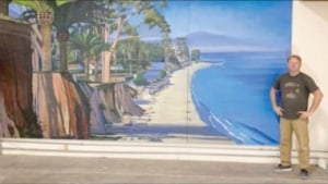 photograph of a man standing to the right of the rediscovered "East Beach to Butterfly" painting by Hank Pitcher