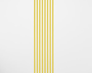 An installation of white gummed paper tape, 8 strips, floor to ceiling, that have a strand of yellow ribbon within each strip.