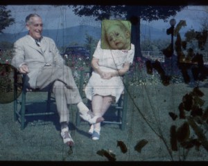 A film still, an elderly couple sitting in chairs on the grass with silhouettes of confetti on the film at right, and a baby image added on top of the female sitter's face