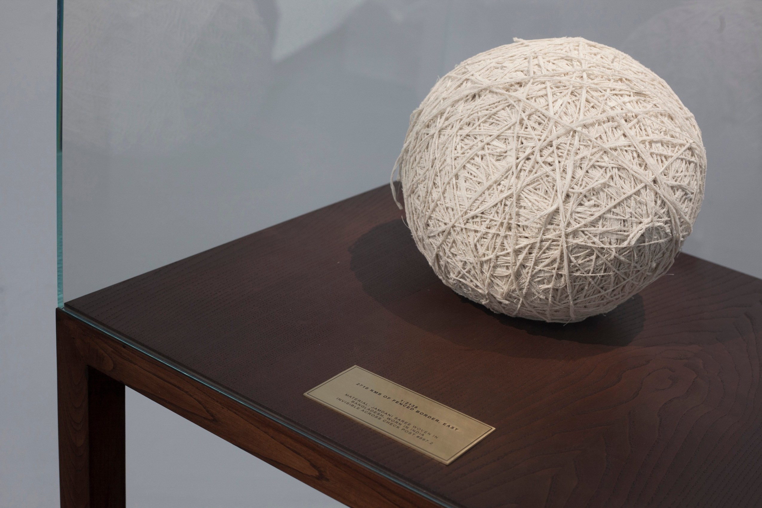 Shilpa Gupta,&nbsp;1:2138 ,&nbsp;2017,&nbsp;Vitrine, brass plate, shredded garment,&nbsp;22 x 20 x 62 in