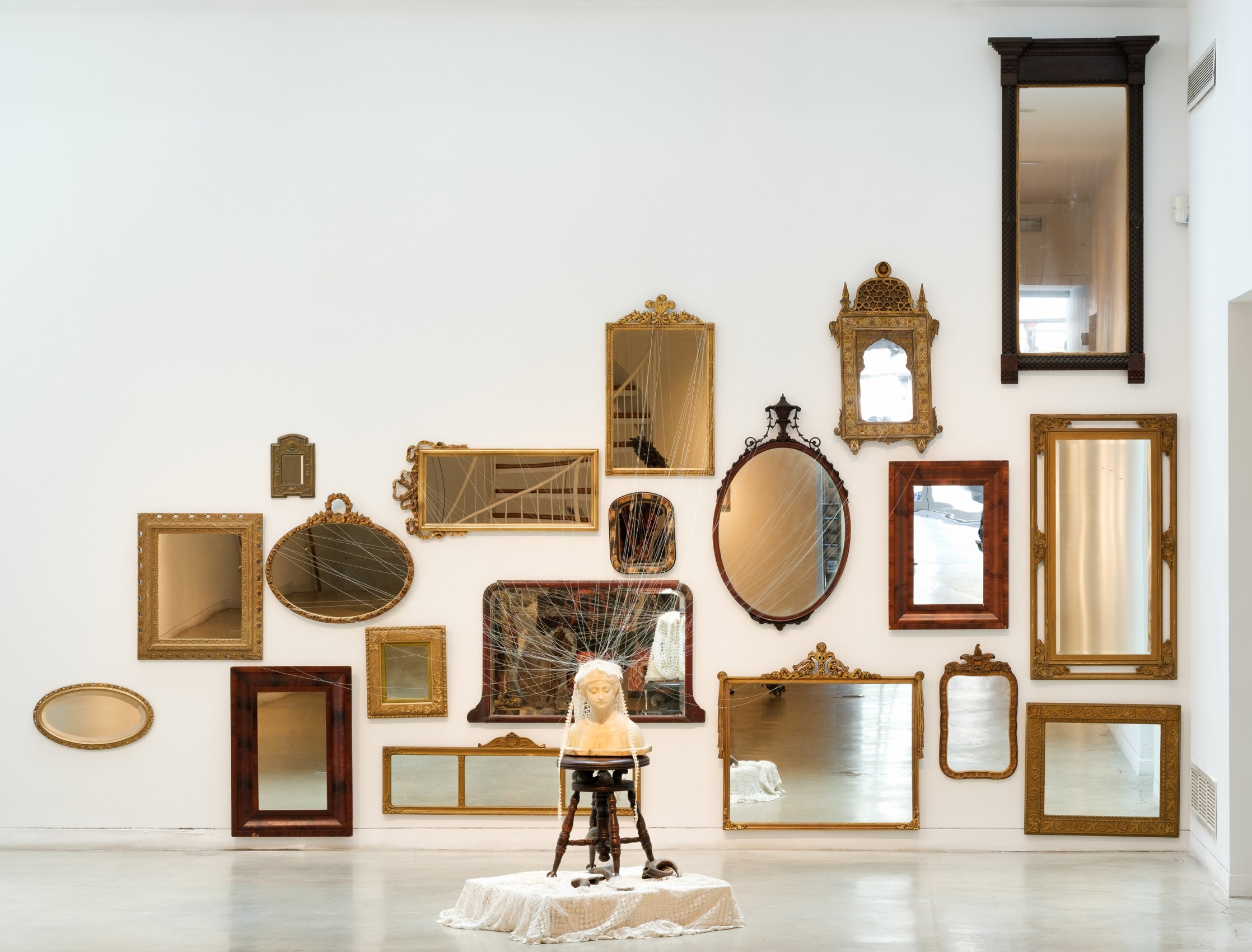 Rina Banerjee, She would be a vision of Beauty if only...her complexion was whitened! As if to not to see her and separately see part of her only not as human body as not yet whole, not yet made, as illness, as a single flaw with intent to take away, save it with this so to cure( vanish cream) her of ugliness, oldness, blemishes, freckles, moles and race deliver her as a sign of brightness, lightness, crowned beauty is a defining system. Where her otherness could marked, has been crowned.,&nbsp;2019,&nbsp;Antique mirrors, cotton thread, alabaster bust, antique lace, antique piano stool, mesh grocery bag, buffalo horns,&nbsp;Dimensions variable