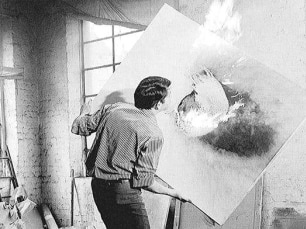 black and white photo of Otto Piene holding a burning canvas as he makes a fireguache