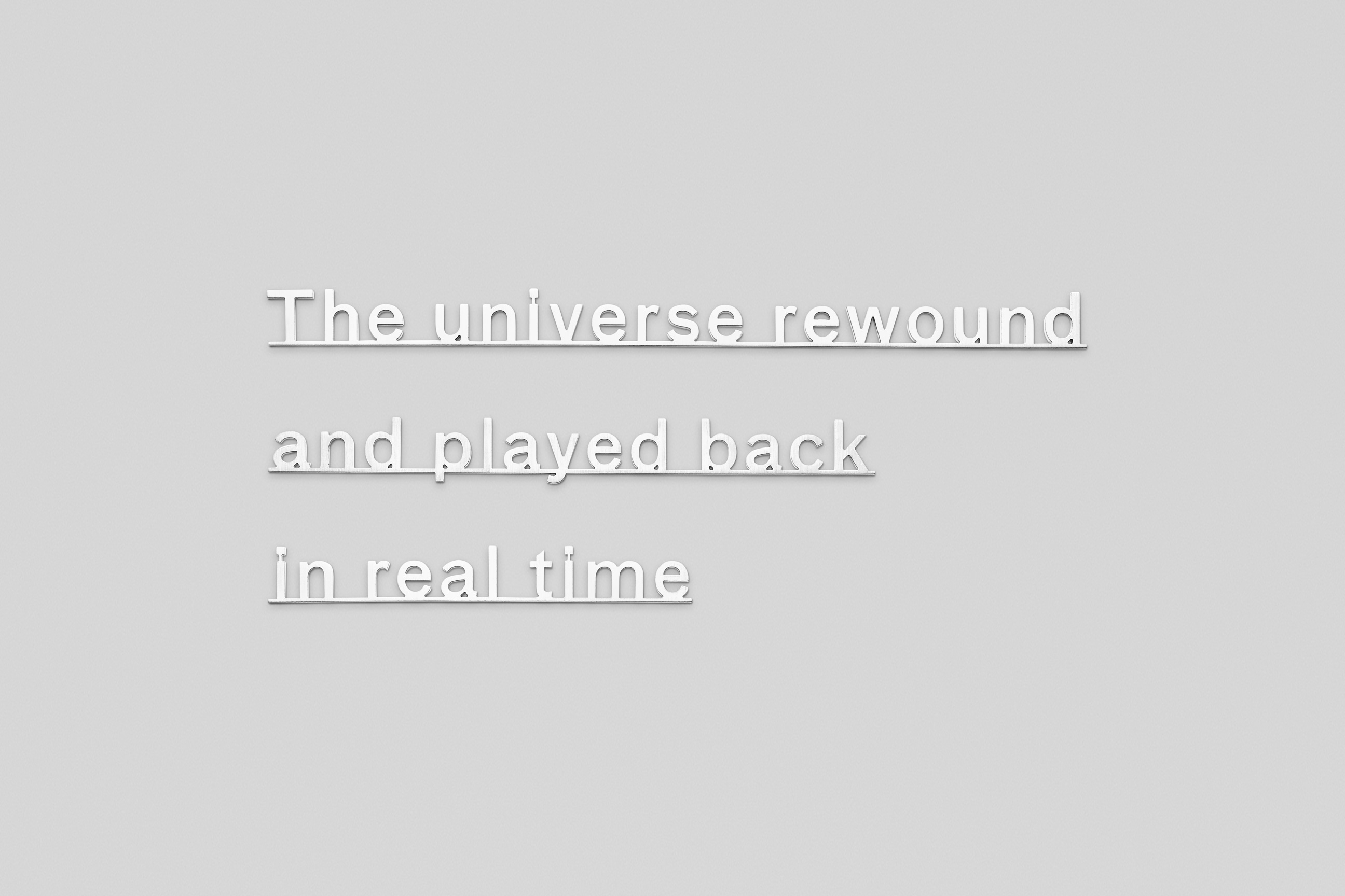 Silver letters on a wall that read: &quot;the universe rewound and played back in real time&quot;