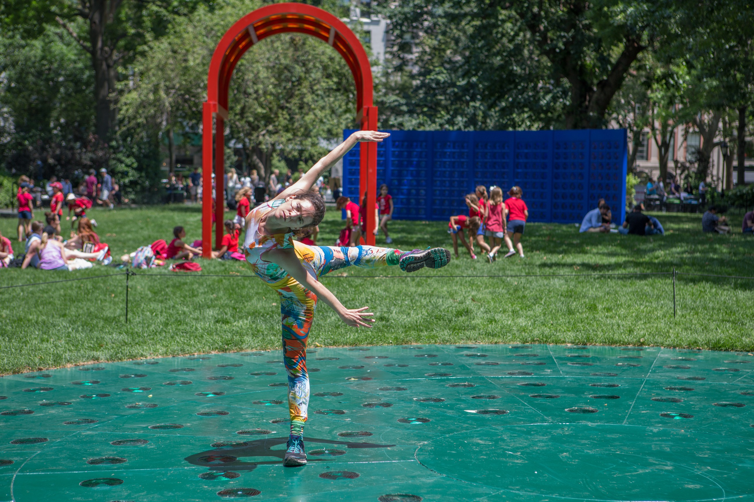 Woman performs in twisted body form in front of the red and blue public sculptures
