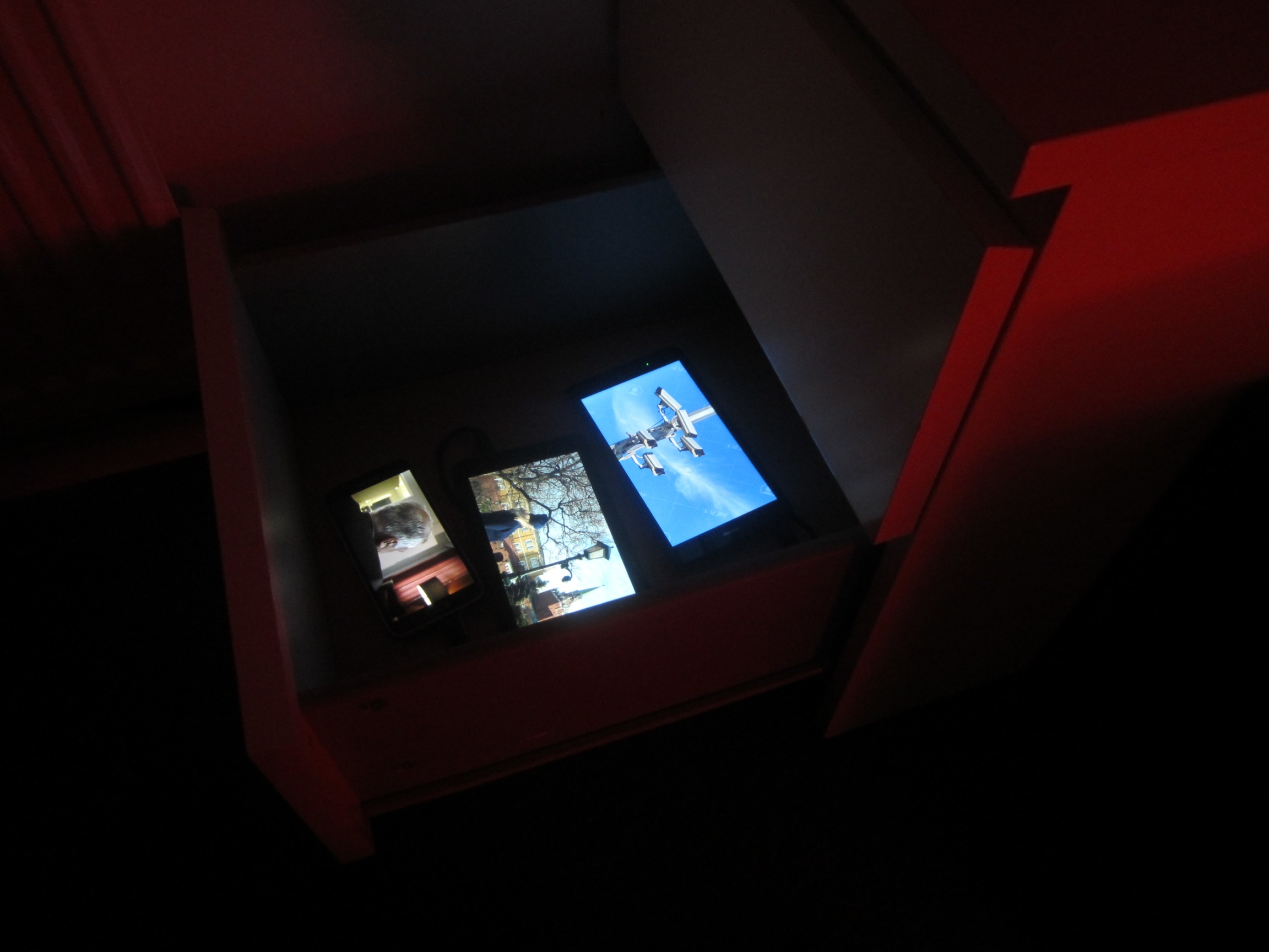 Image of an artwork installation that features 3 mobile phones inside a desk drawer