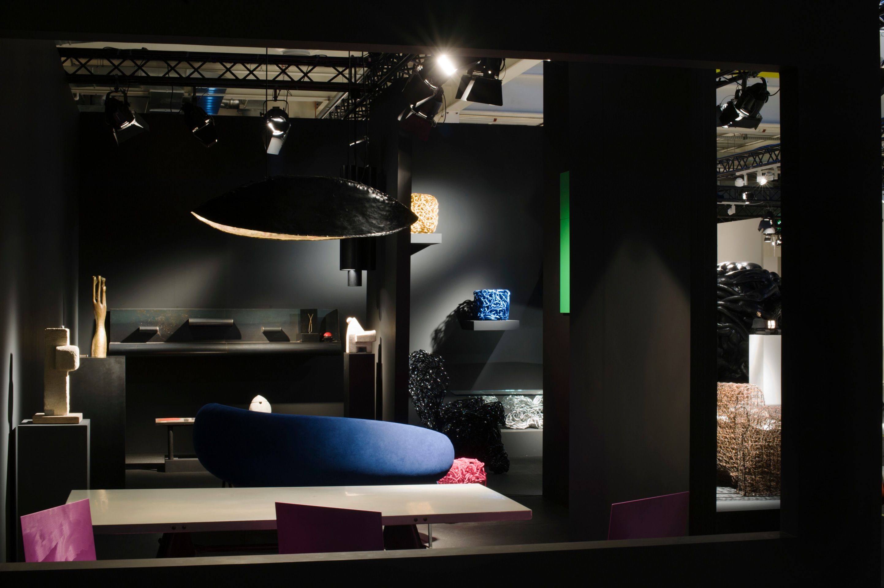 Magen H Gallery's booth at Design Miami/ Basel, installation view of booth, showing Pierre Sz&eacute;kely's hanging light fixture, wall-mounted metal console, and back of boomerang shaped sofa