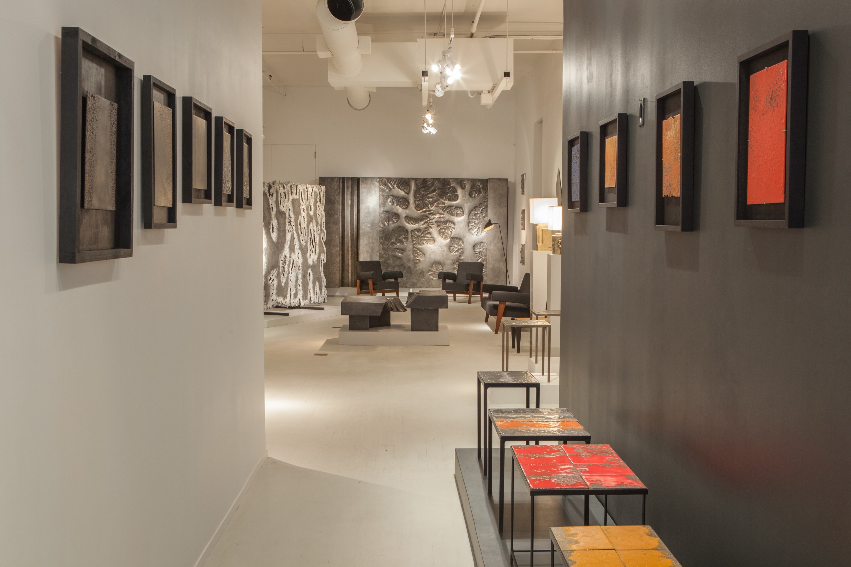 Pierre Sabatier exhibition installation view of the entry way displaying a line of wall sculptures as well as volvic side tables