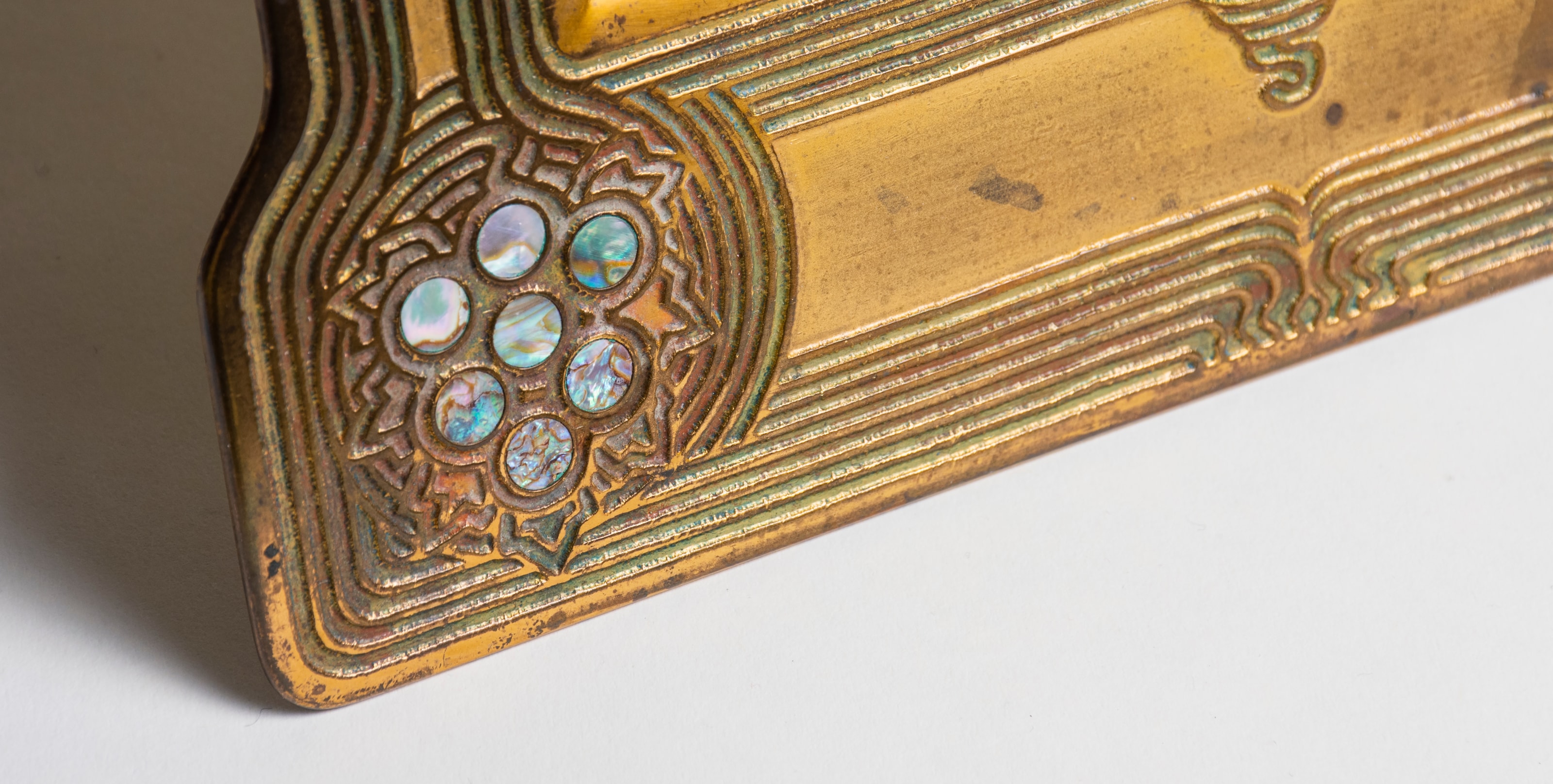 A detail showing the tiffany abalone picture frame's lower edge, showcasing the grape motif of inset abalone shell and the inset lines of enamel which look like grape vines.