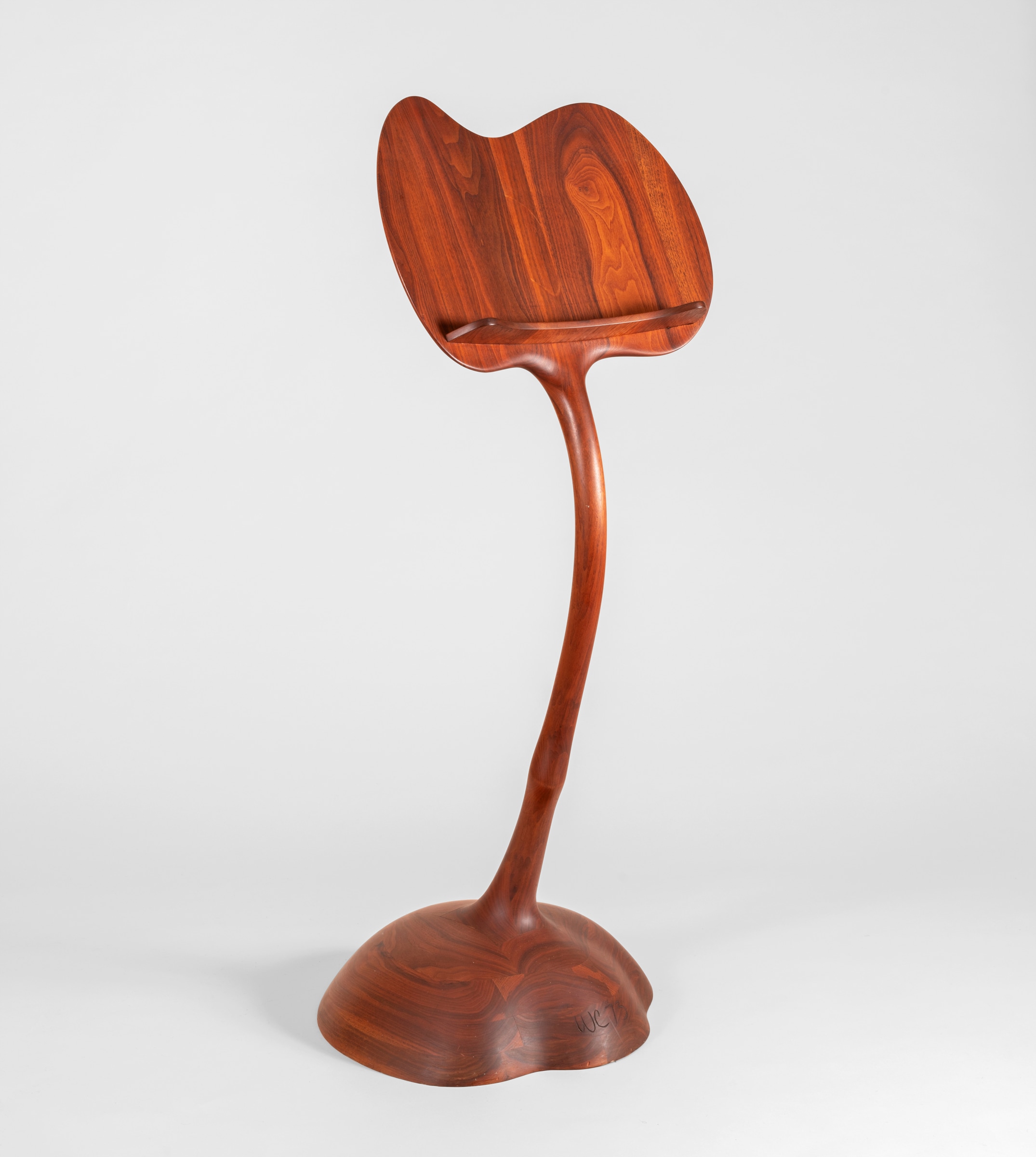 a stacked and laminated carved wooden music stand by wendell castle, rounded biomorphic forms, the cloudlike base supporting a thin stem with a knob vaguely resembling an animal's leg.