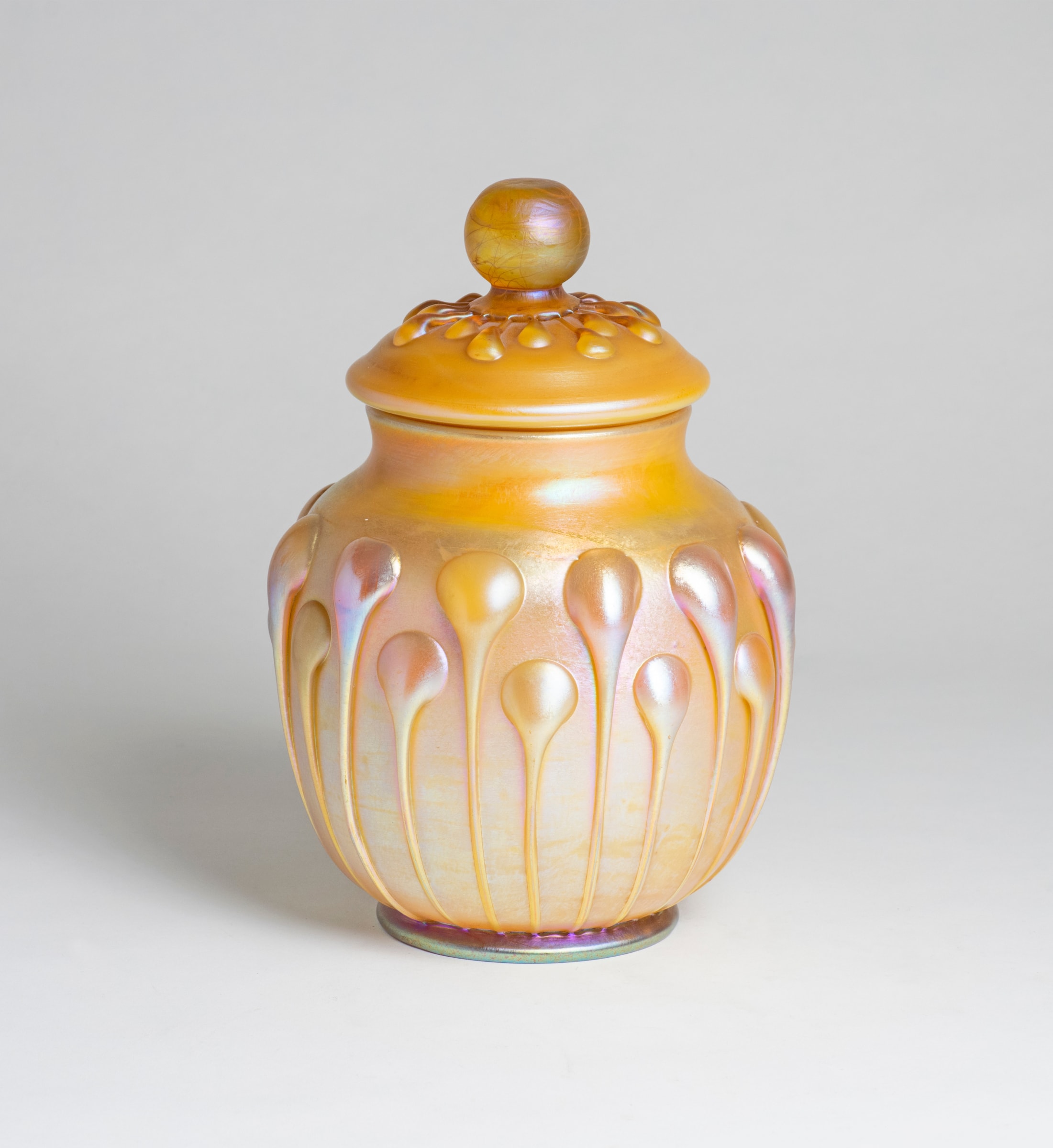 A gold iridescent Tiffany Favrile Glass jar with a matching lid, both decorated with matching decoration of applied lily-pad shaped glass drips.