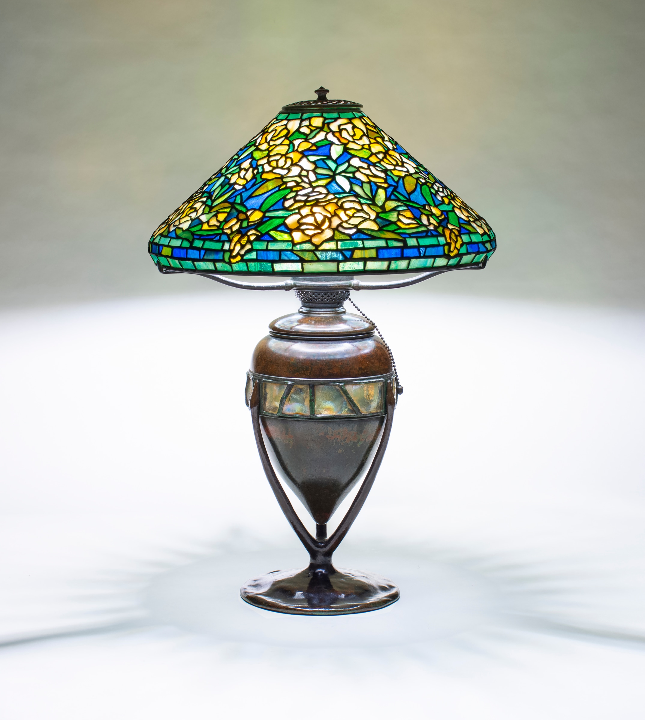 A Tiffany Studios Lamp, with a Wild Rose pattern shade with mottled yellow flowers against a deep blue sky, paired with a bronze table base in brown patina, the body with a horizontal row of inset Tiffany Favrile Glass Turtle Back Tiles with uneven gold iridescent surfaces.