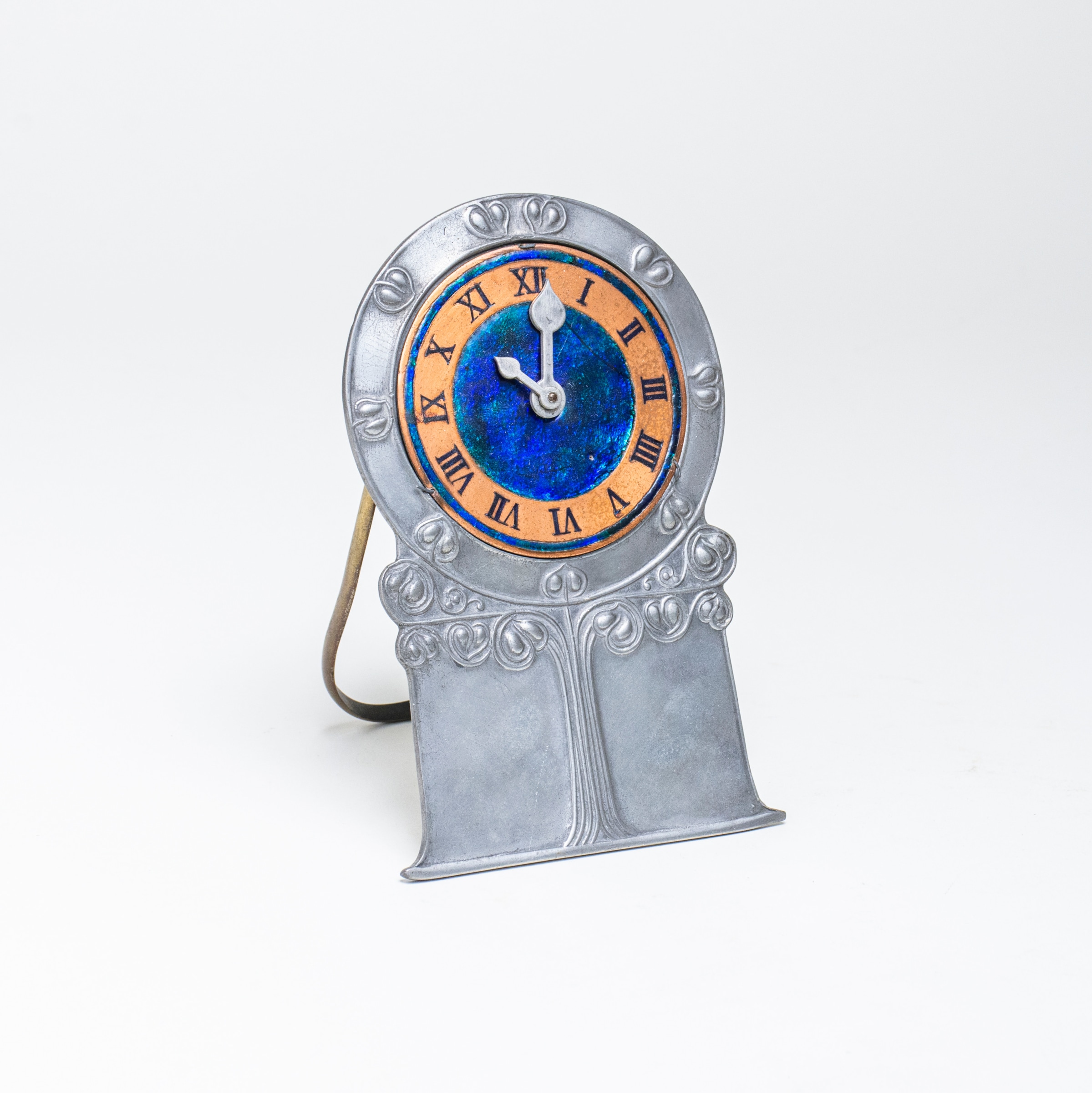 a pewter or tudric clock by liberty &amp; co with tulip repousse motif in art nouveau style and blue enamel decoration, possibly by archibald knox