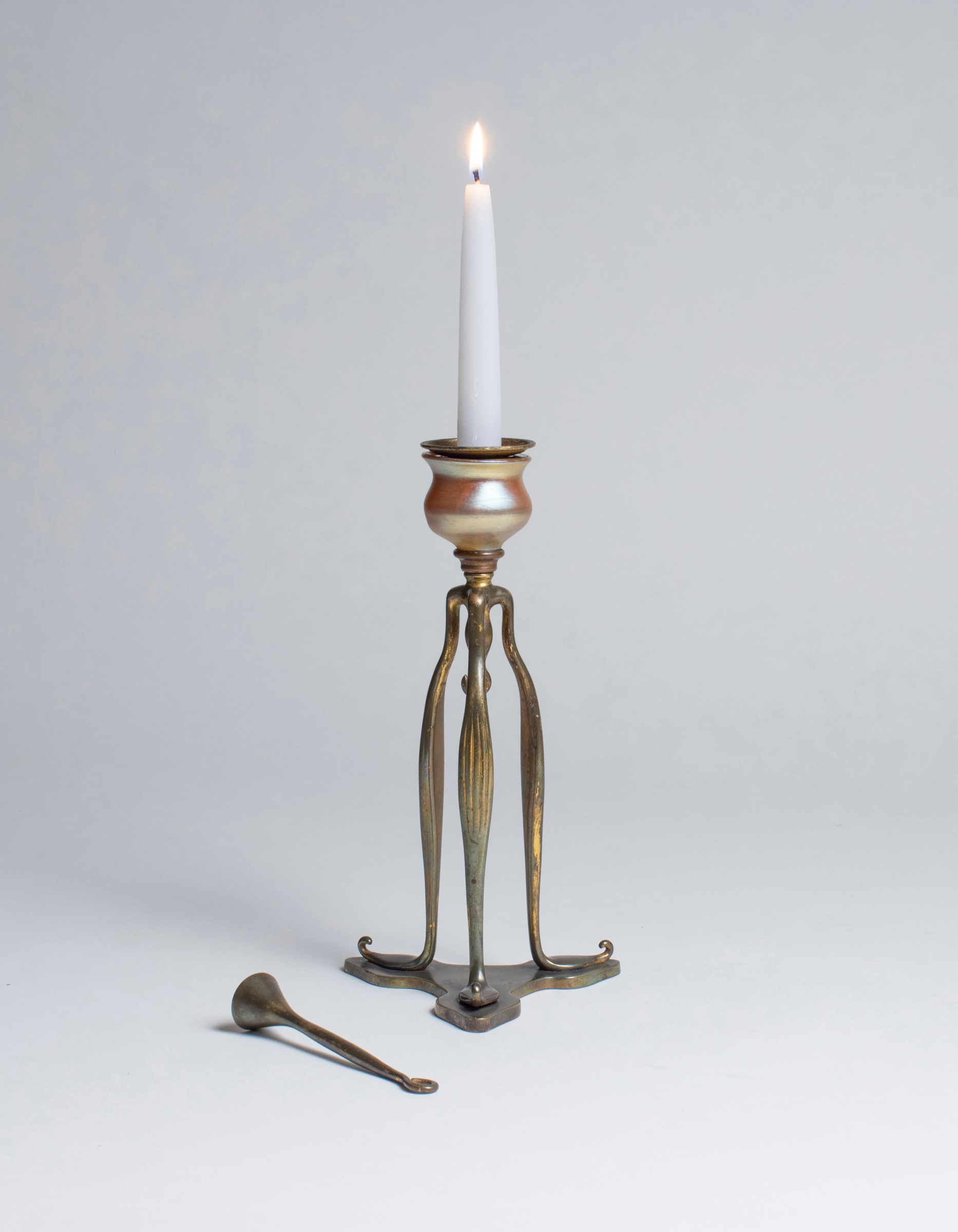 A tiffany studios candlestick, the bronze tripod form with a gold iridescent finial as part of the candle cup.