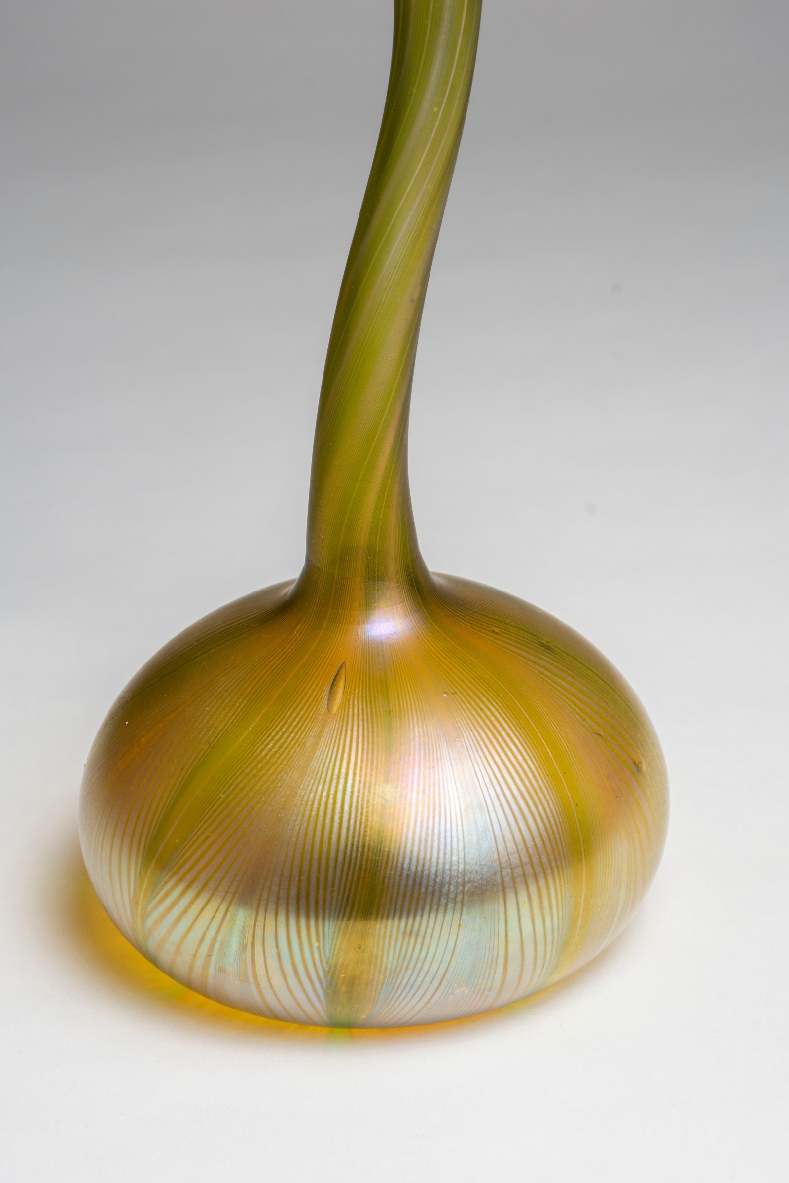 the round foot of the tiffany favrile glass rosewater sprinkler or gooseneck vase, showing the thin striations of the pulled feather decoration against the gold iridescent tiffany glass