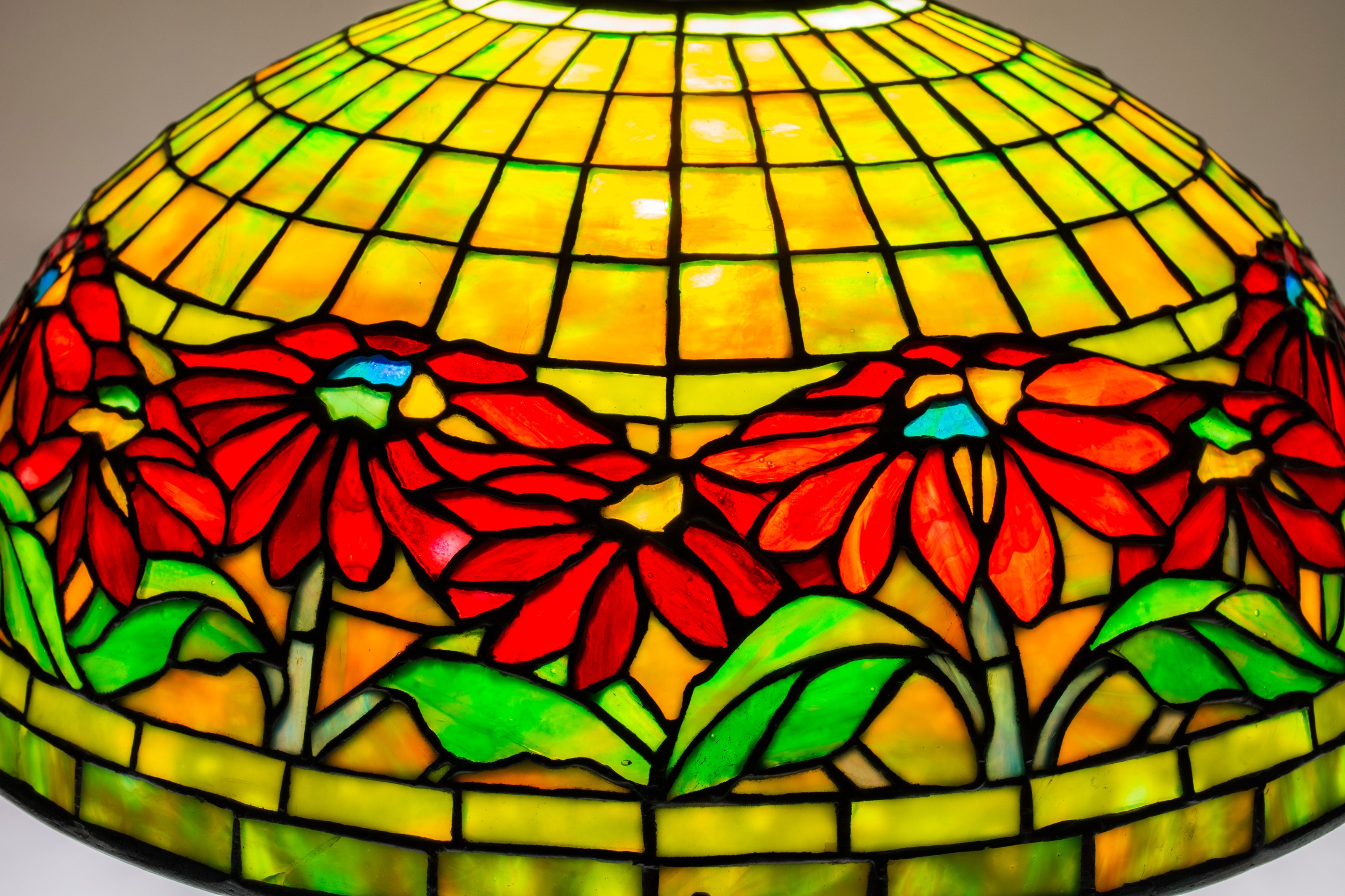 a tiffany lamp with leaded glass shade, the domed shade formed by horizontal leaded glass in a gridded pattern, in yellowish green, with a horizontal border of floral decoration depicting red poinsettias