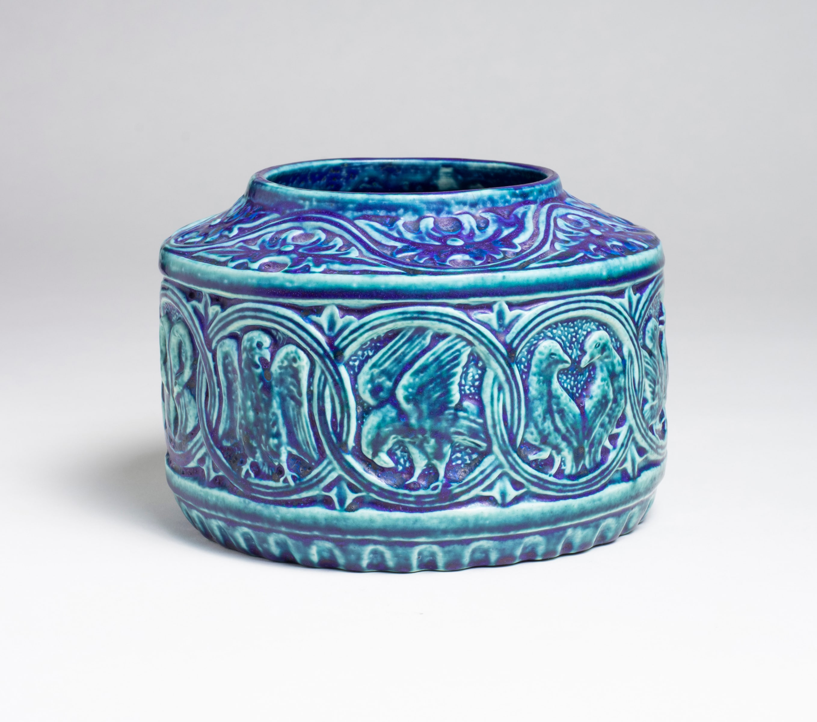 a favrile pottery low bowl by tiffany studios, in a variegated blue glaze, the flat horizontal frieze-like band at the center decorated with a motif of interlaced circles, each containing a different image of a bird of pair of birds