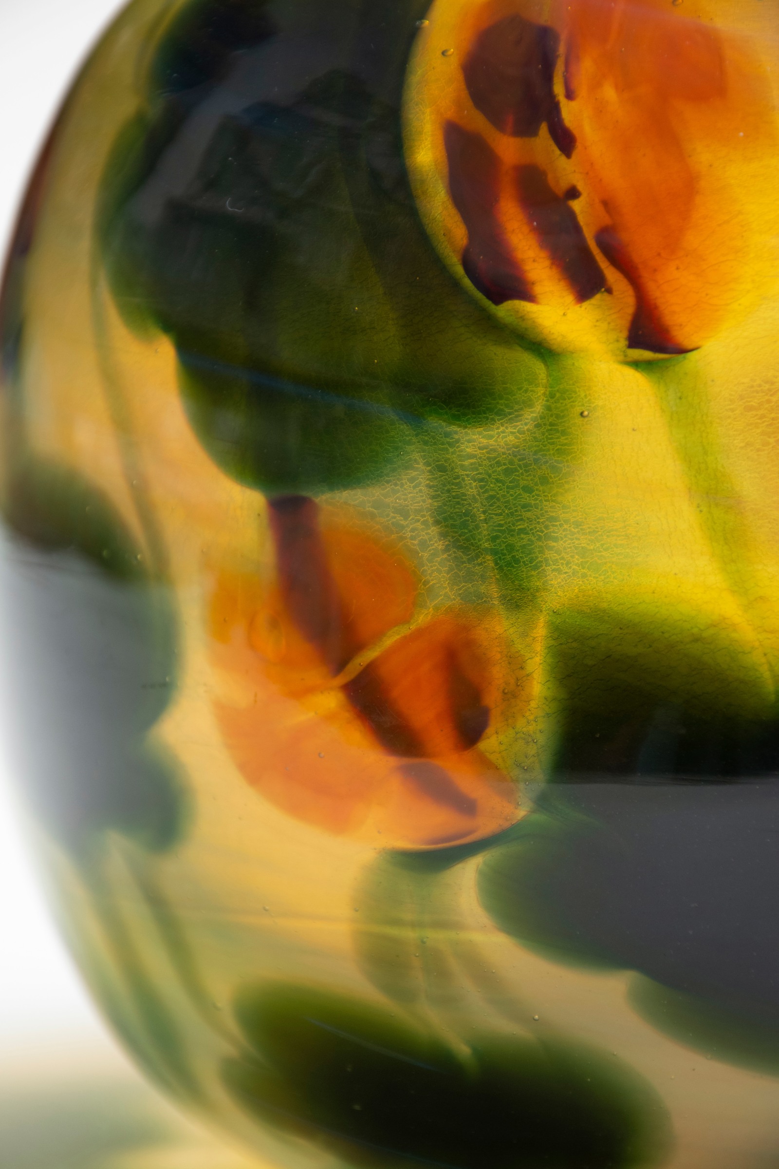 a detail shot of the tiffany favrile glass nasturtium paperweight vase, showing how the red flowers are floating above the layer of leaves and vines, which are above the background layer of glass. All of it is encased in a clear layer of glass.