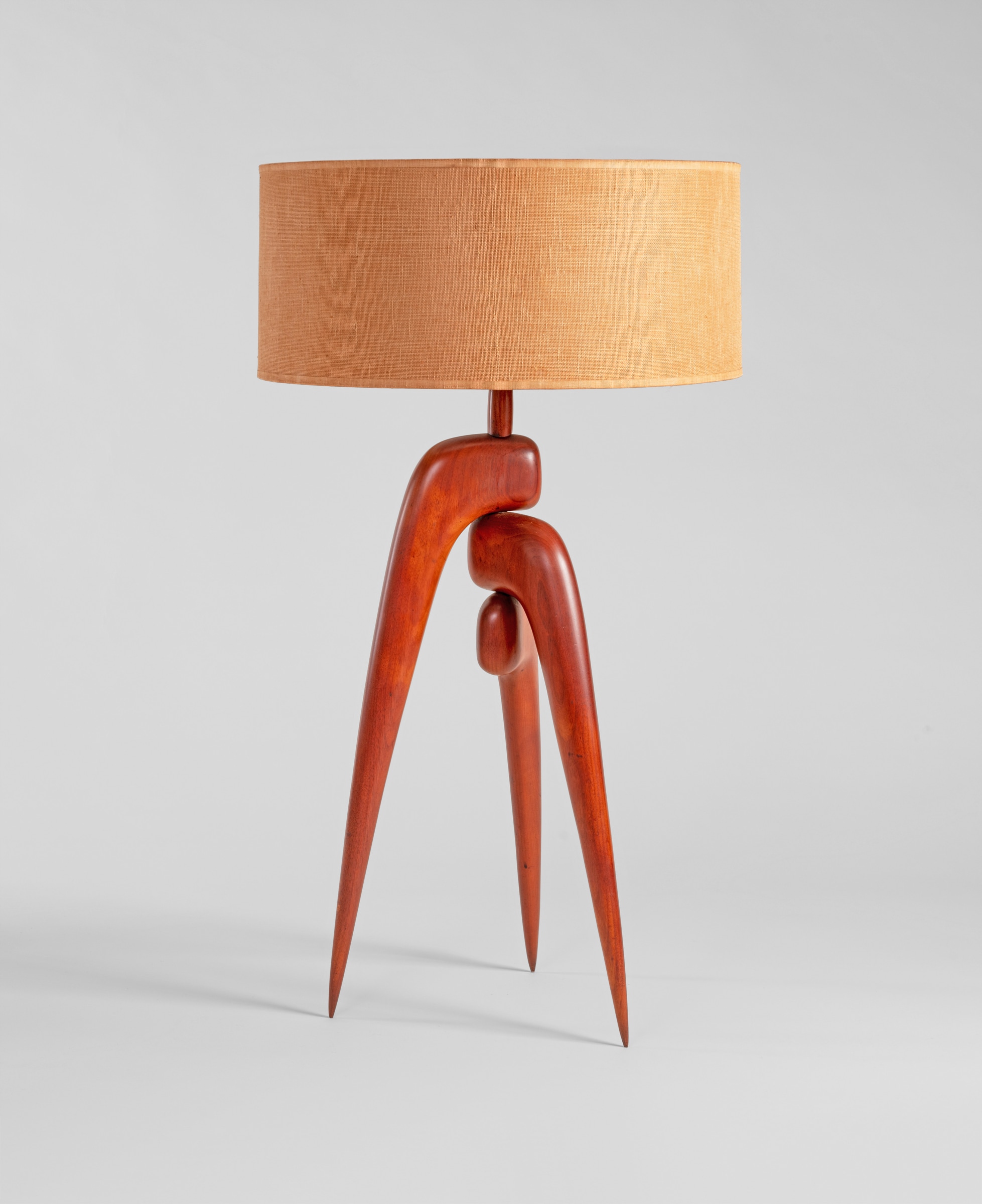 a rare midcentury modern table lamp by new hope designed phil powell, the wooden base an unusual sculpted tripod of rounded forms, supporting a round linen shade in natural tone