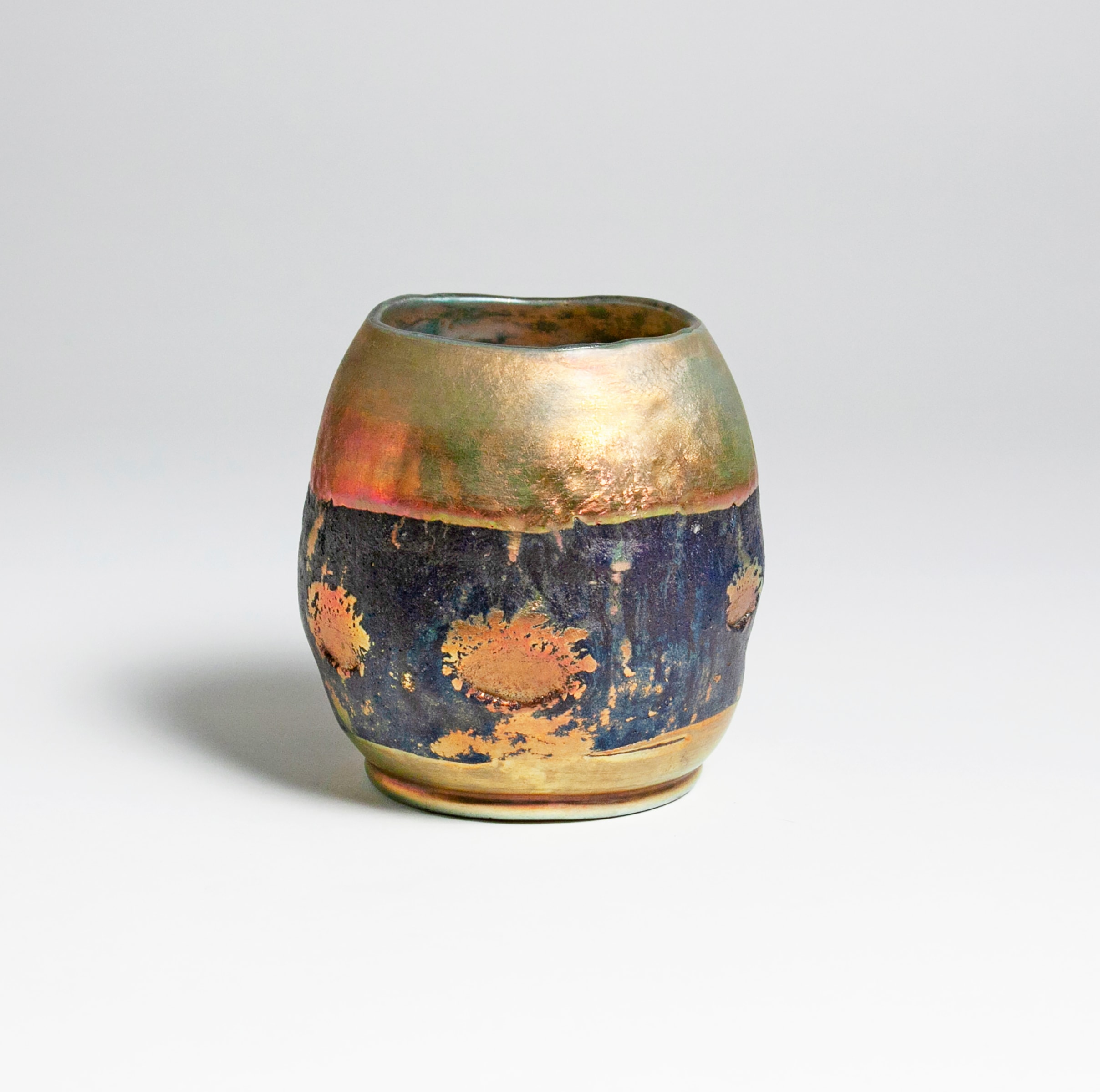 a rare tiffany studios lava favrile glass vase, short irregular cylindrical form recalls japanese raku tea bowls. The body of the vase in gold iridescent glass, a horizontal band of rough textured black matte glass at the center featuring a row of splattered dots of glass in the same gold iridescent.