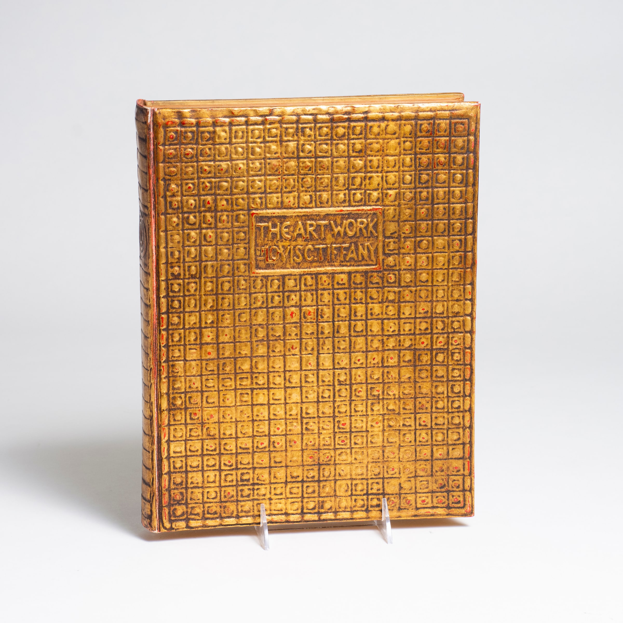 an art book, a biography by charles de kay of louis comfort tiffany, the cover in embossed gilded papier mache in a pattern of raised squares