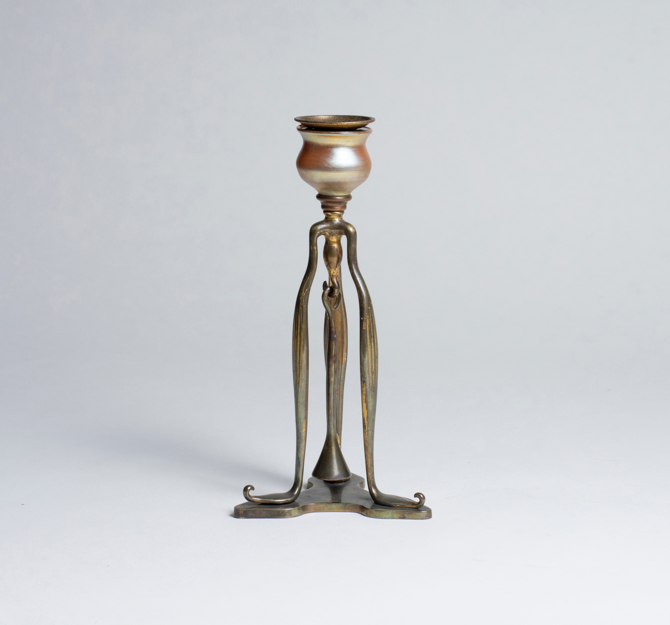 A tiffany studios candlestick, the bronze tripod form with a gold iridescent finial as part of the candle cup.