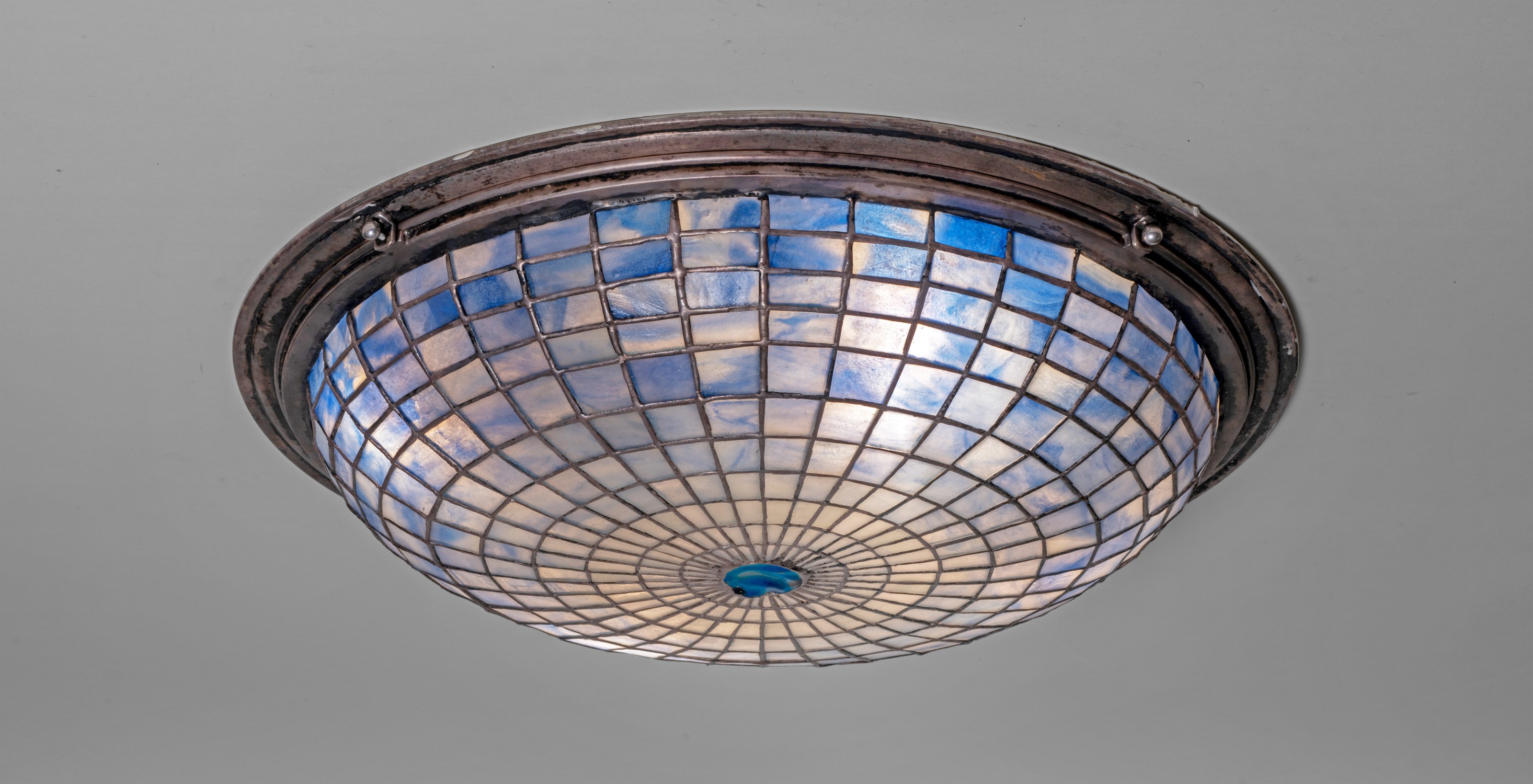 a rare ceiling light fixture by tiffany studios, the shade formed by a flattened dome of leaded gridded glass with a round iridescent blue tiffany glass tile at the center, with silver leading