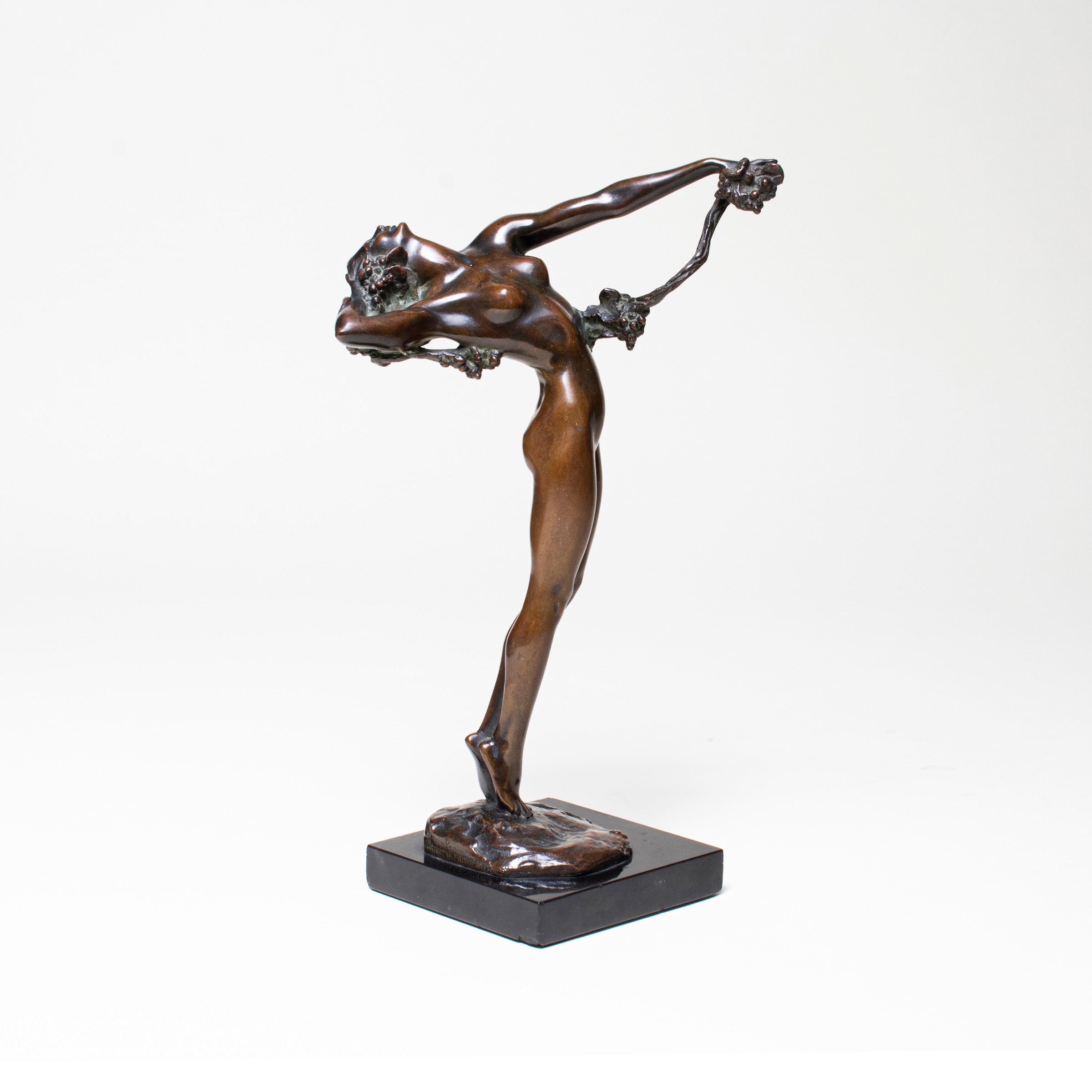 a sculpture of a young woman standing on two toes, leaning back in an acrobatic position, holding aloft a thin vine with grape cluster sin one hand, the other pulling back her swinging hair.