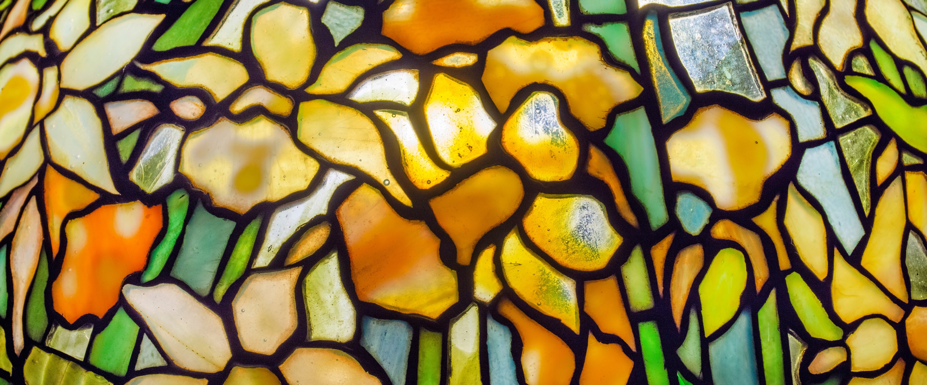 leaded glass tiffany lamp depicting daffodil blossoms in mottled yellow with spiky greenish blue leaves against a transparent glass background