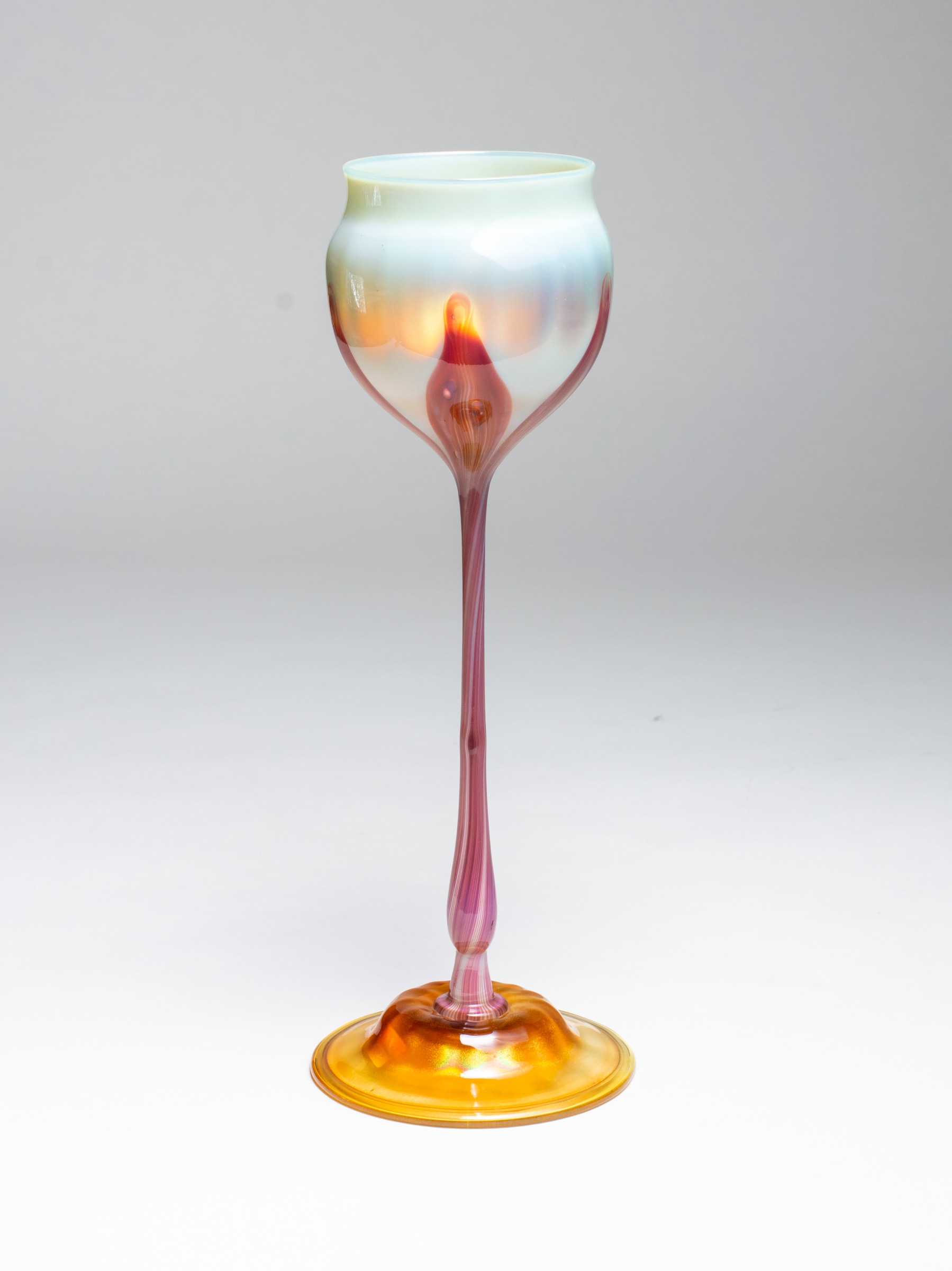 an early tiffany favrile glass flower form, the creamy white flower cup supported by a stem of deep red glass, on a domed foot. red was an unusual and rare color in blown tiffany glass,