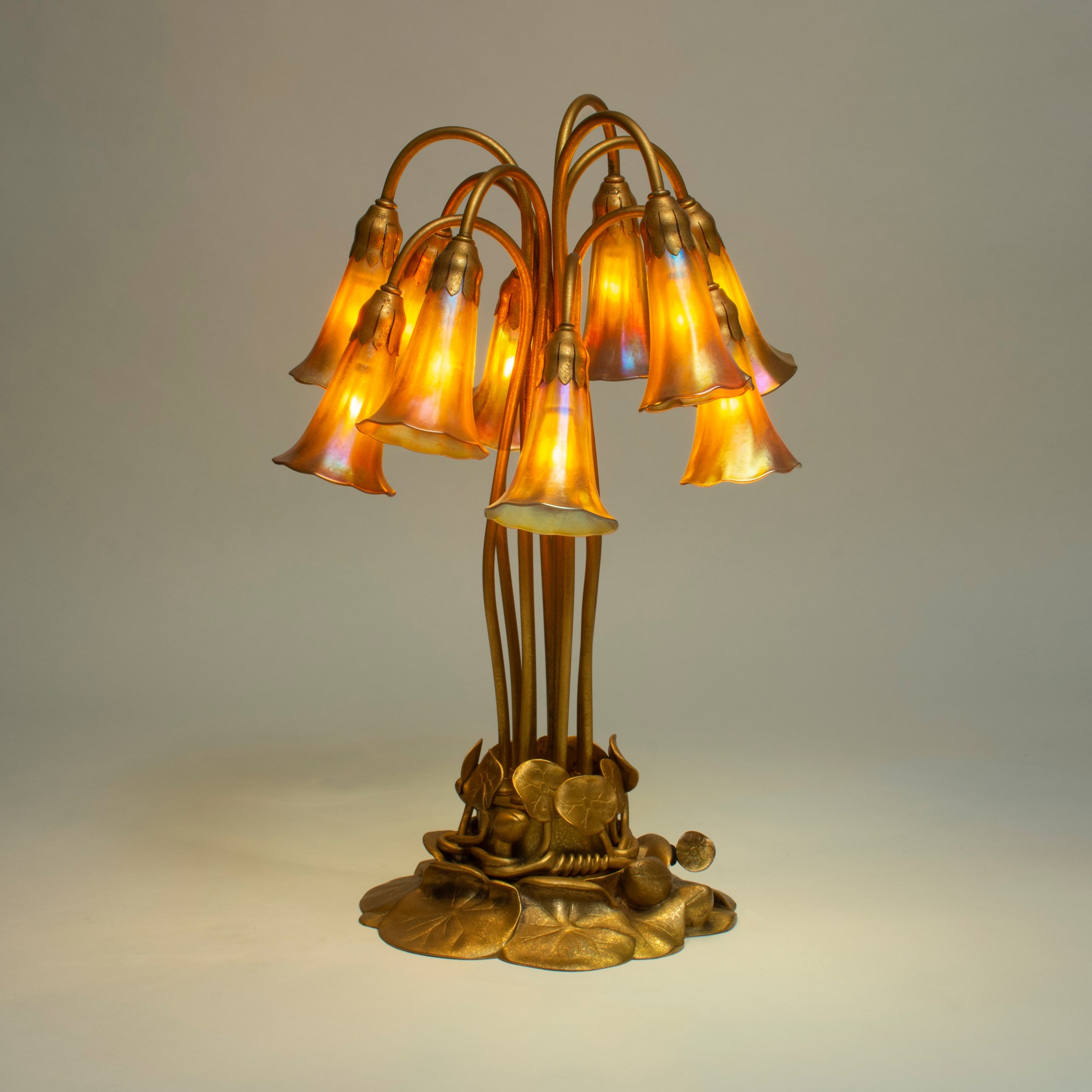 tiffany studios lily lamp - gold patina - illuminated, the gold favrile glass shades providing a rich warm glow.