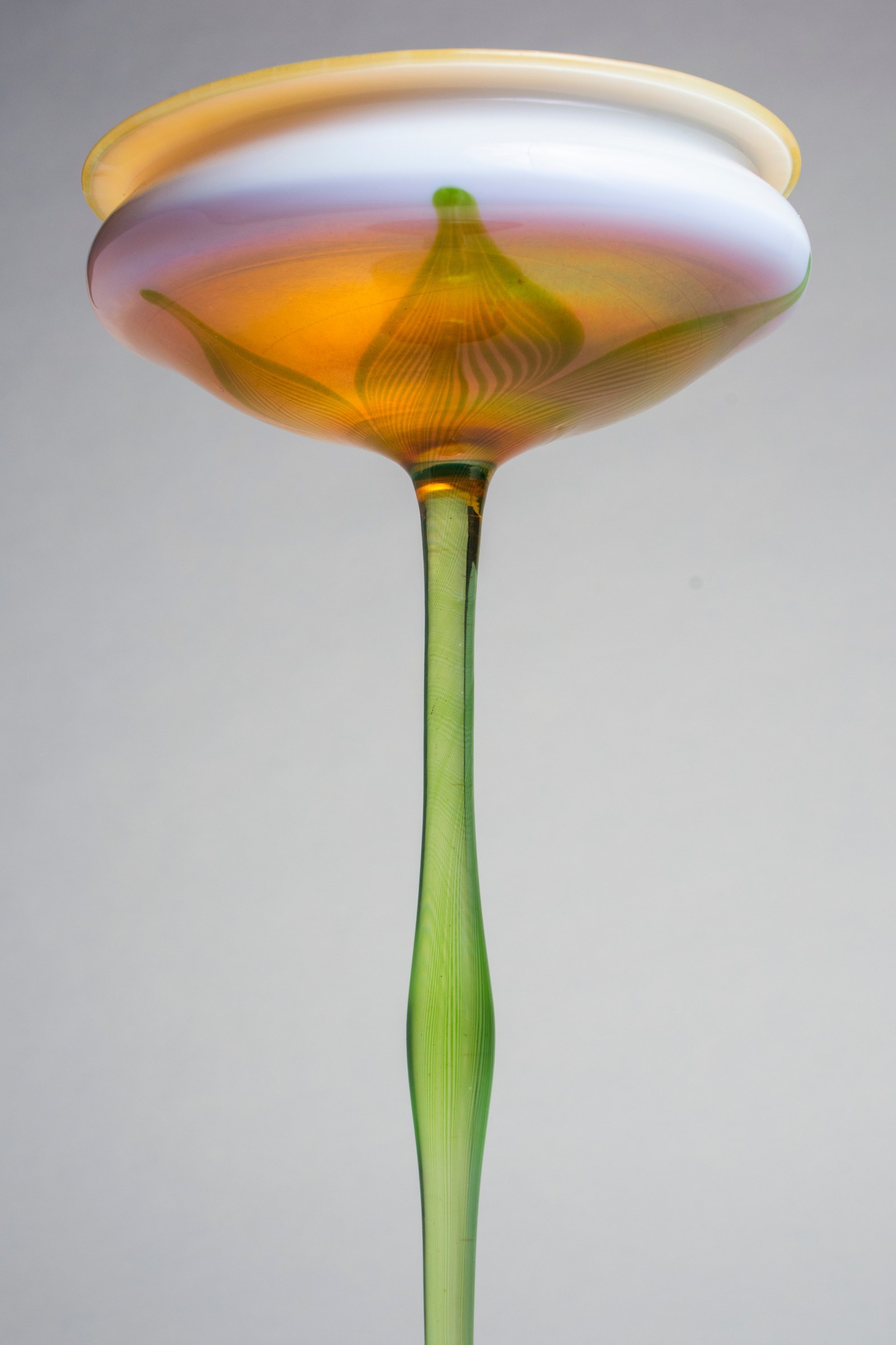 a detail of the tiffany favrile glass flower form's wide mouthed &quot;flower&quot; cup, showing the thin glass stem's striations and the leaf decoration
