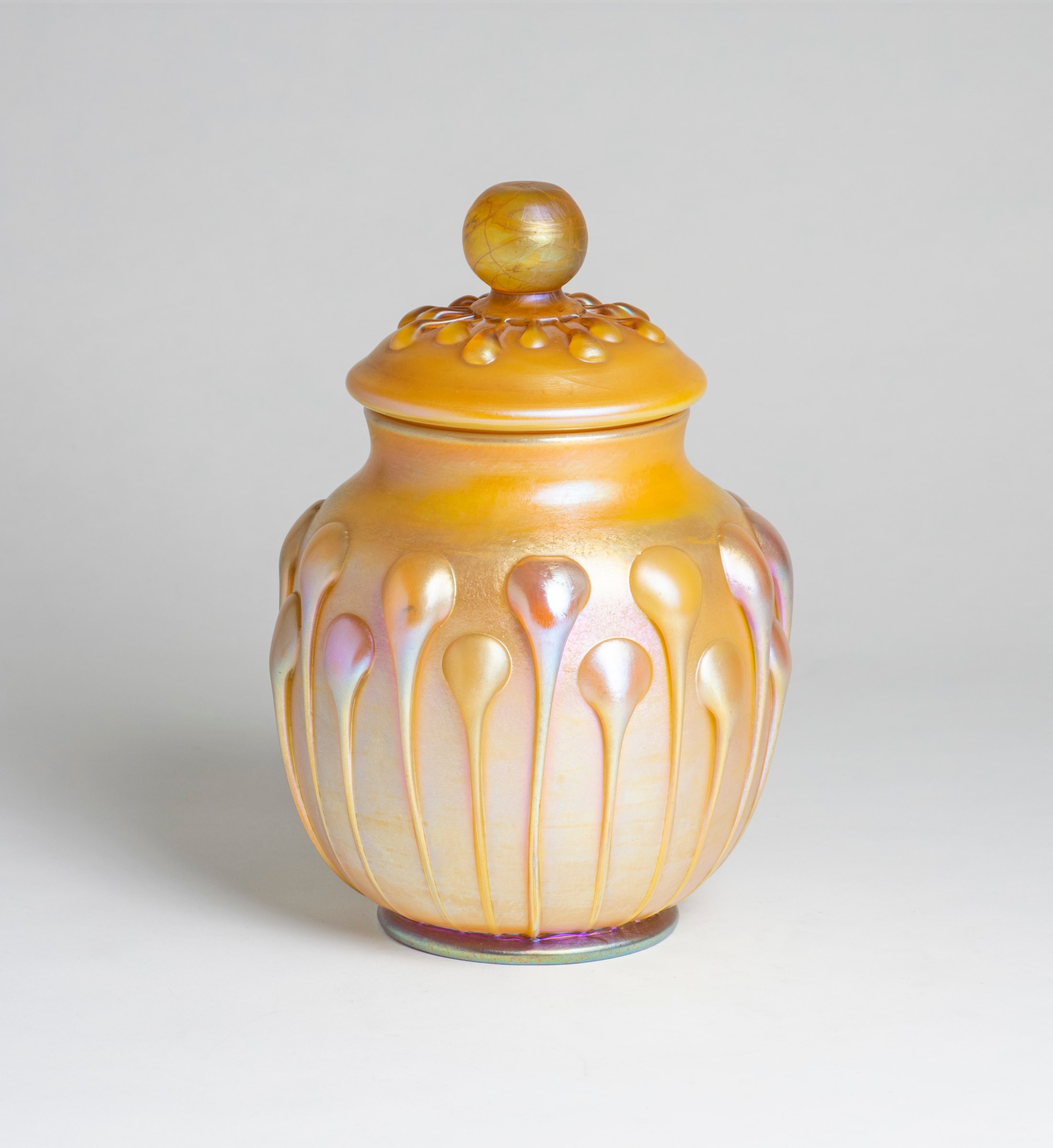 A gold iridescent Tiffany Favrile Glass jar with a matching lid, both decorated with matching decoration of applied lily-pad shaped glass drips.