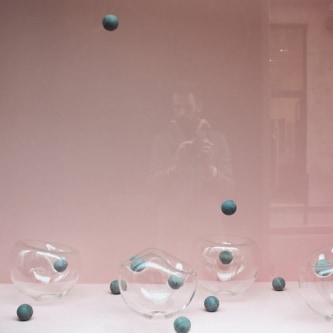photograph of a display case with pink wallpaper containing amorphous glass spheres and concrete balls