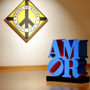 Installation view of the exhibition Robert Indiana at Galleria d'Arte Maggiore, Bologna, Italy with a blue and red AMOR sculpture and the painting Where Oh Where Hides Peace