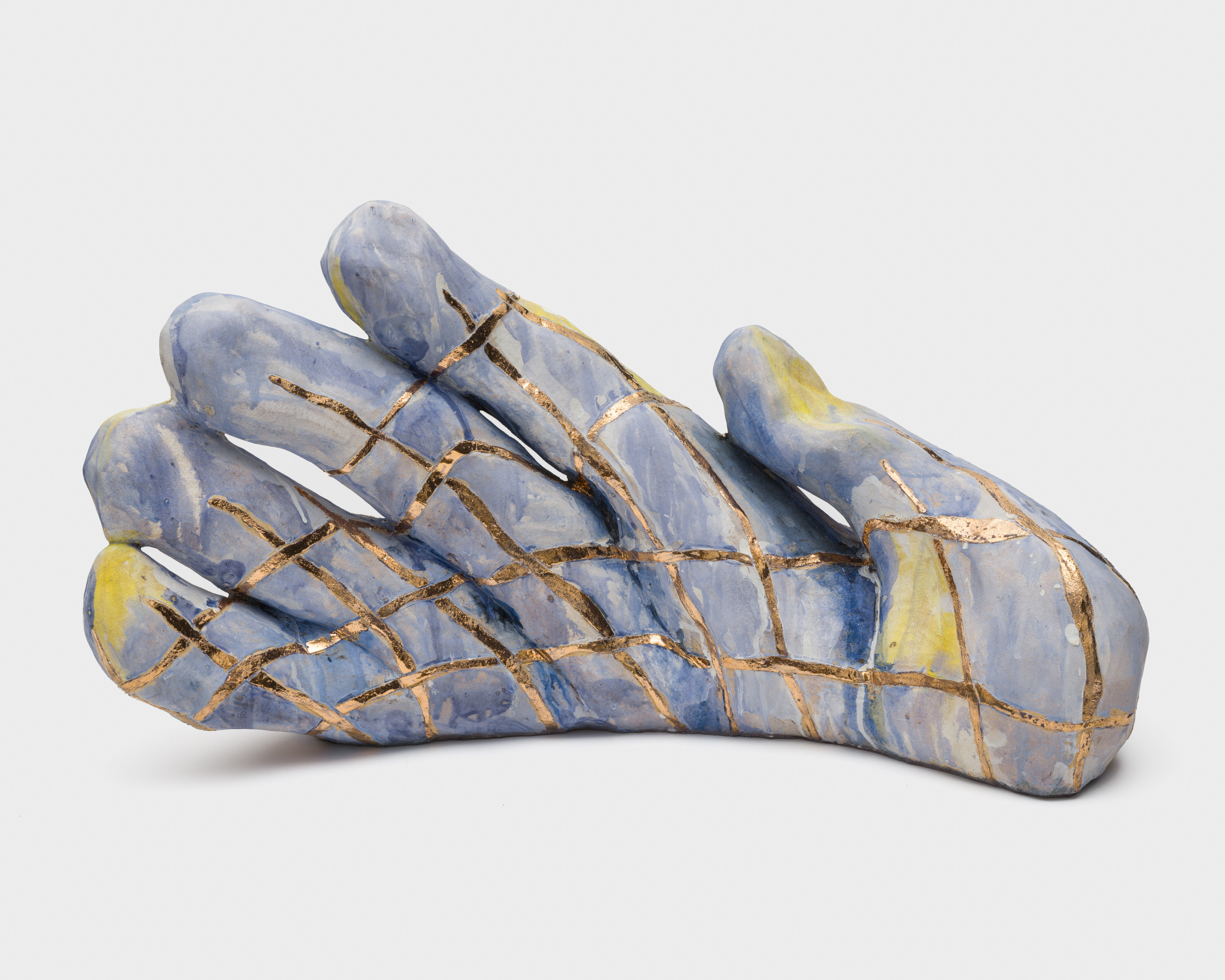 A blue and yellow ceramic sculpture of a hand covered in a golden grid with the fingers extended towards the sky.