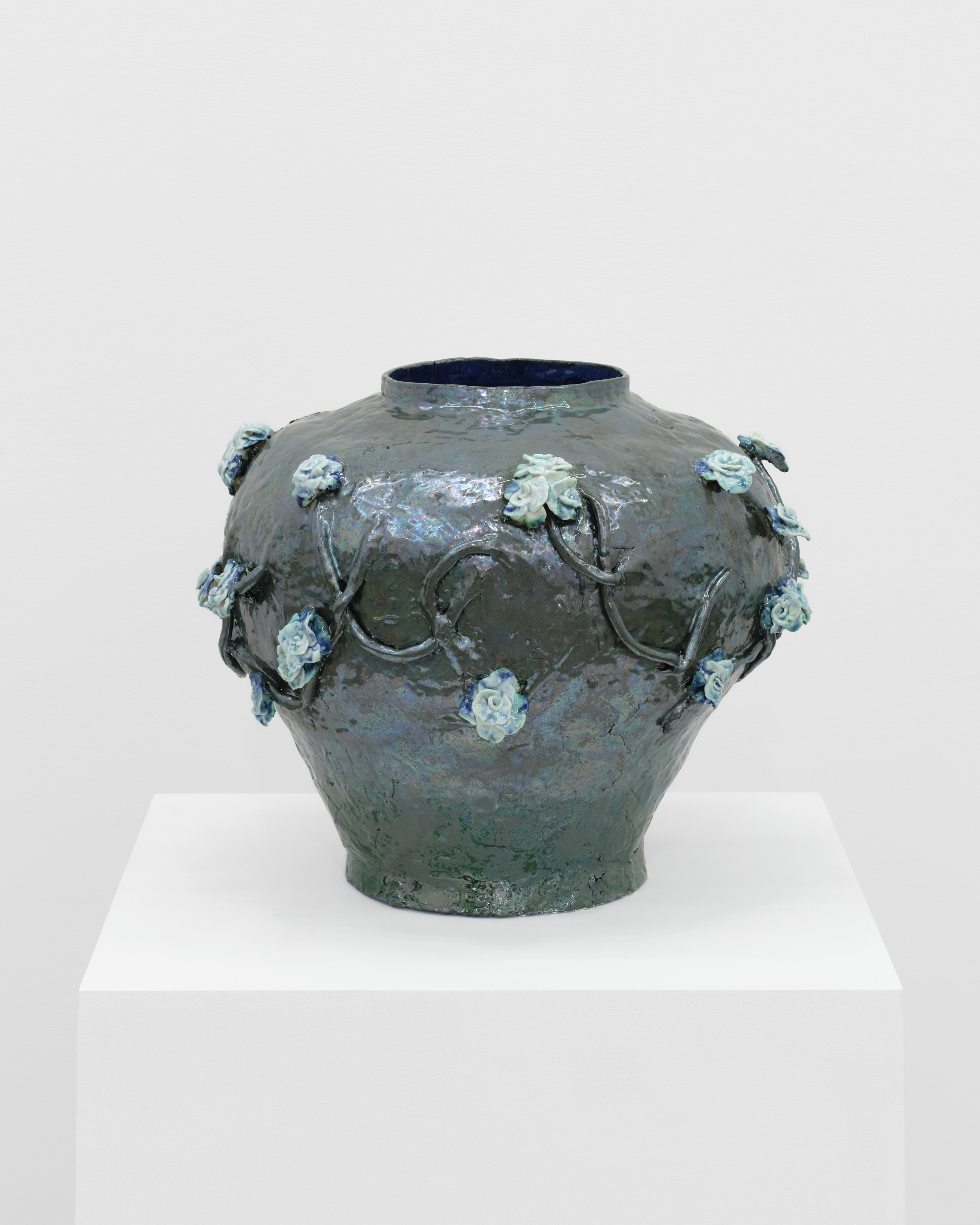 A grey blue round ceramic vessel with ice blue roses strung around the form.