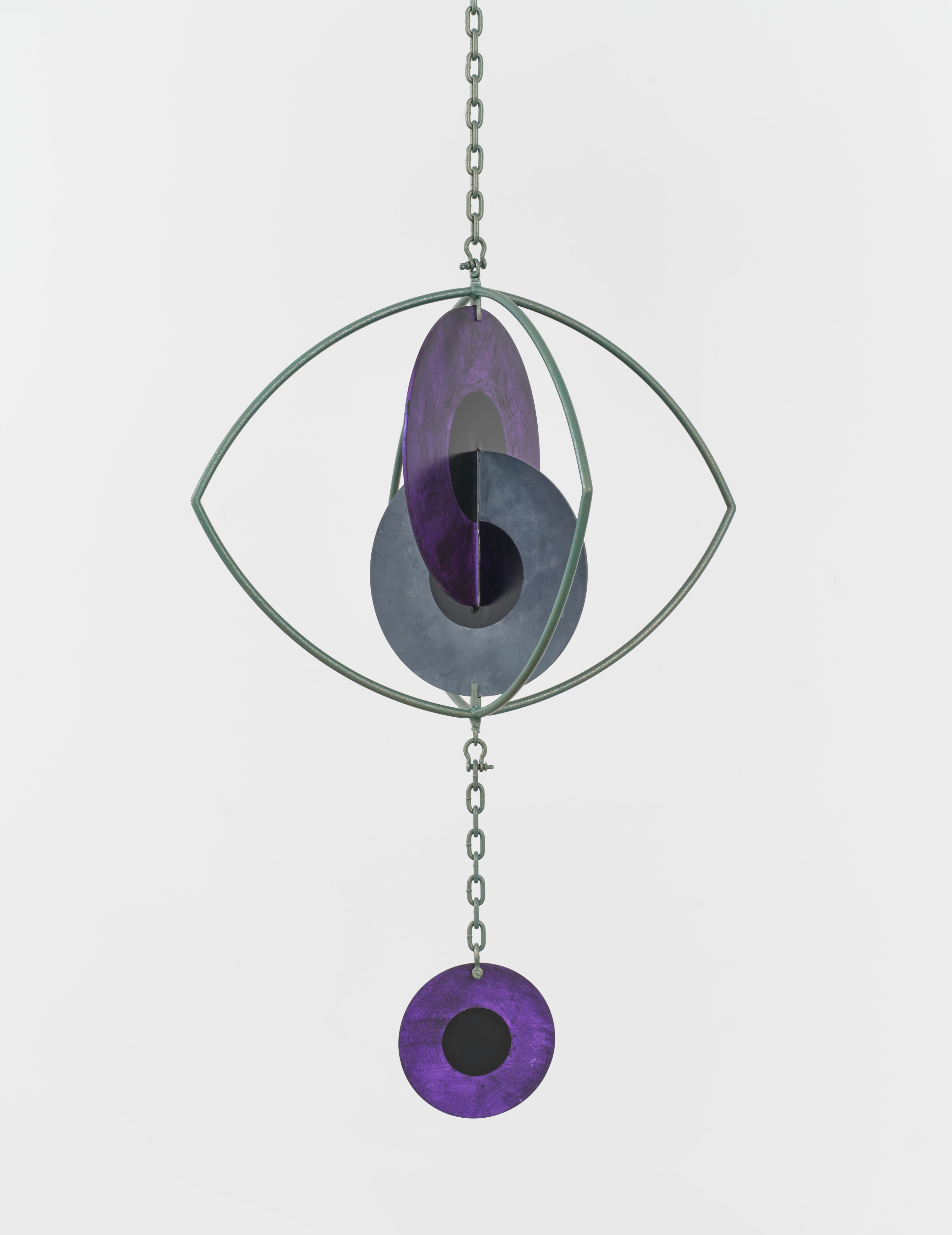 A hanging sculpture with two interlocking metal iris' inside a metal eye with a third iris hanging from a chain. 