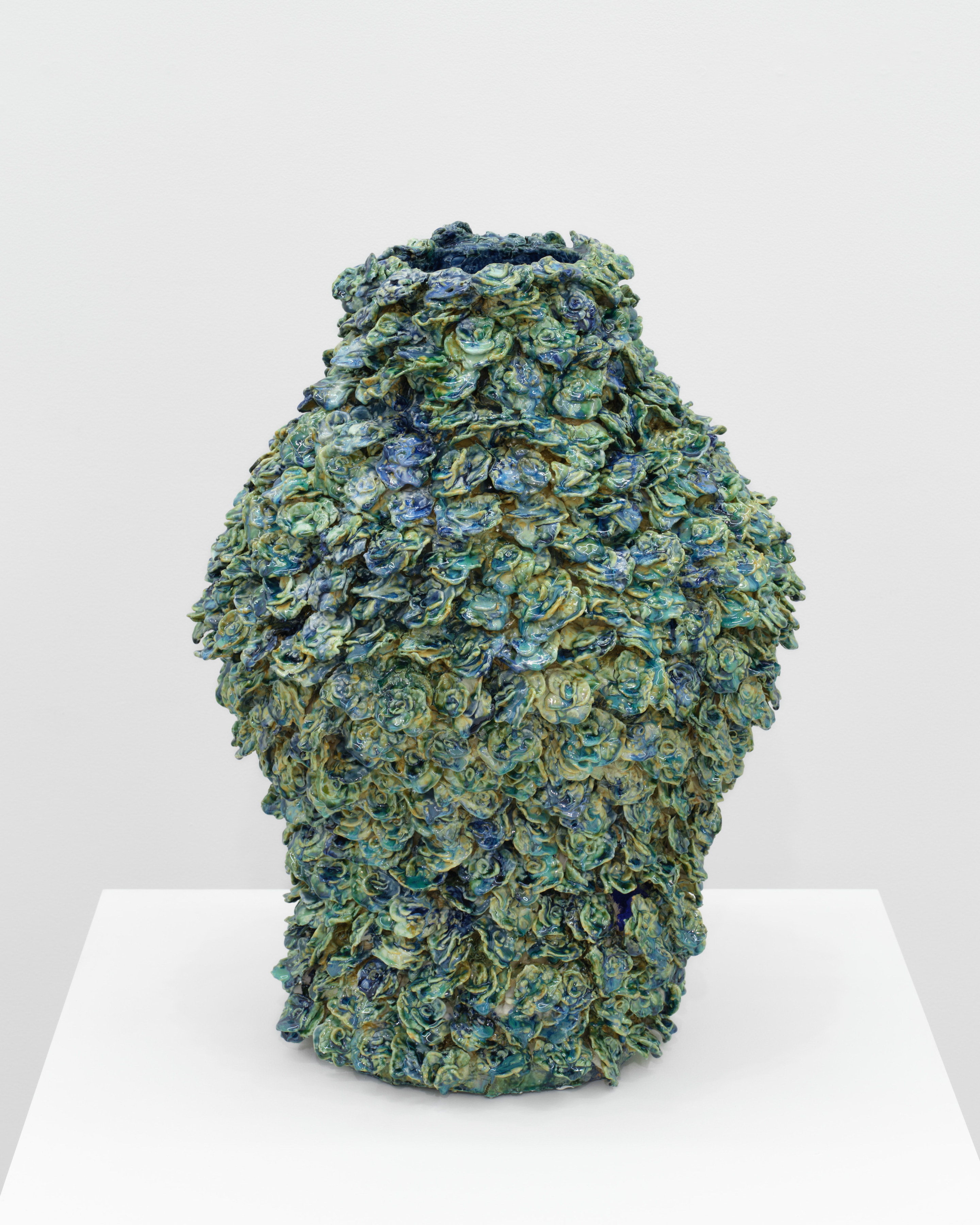 A blue and green ceramic vessel covered in layers of rose like floral shapes.