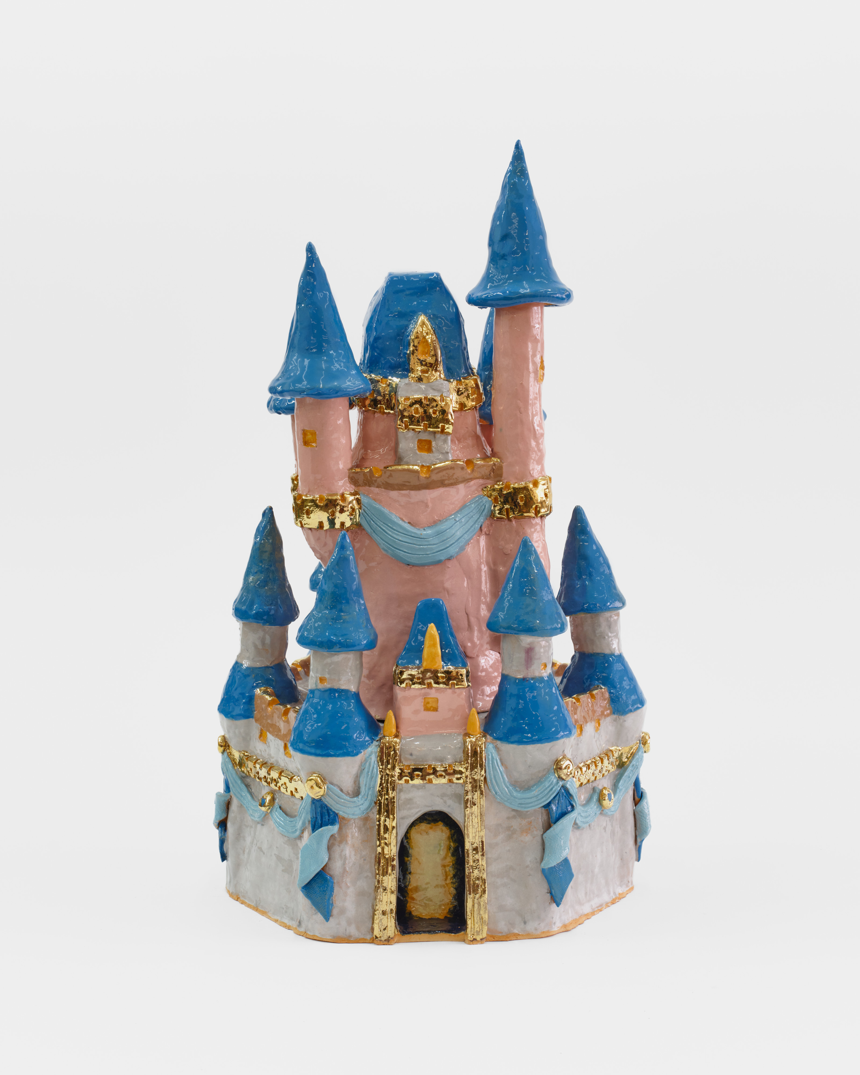 A ceramic sculpture of a Disney like pink castle with blue tipped turrets, ribbons and golden features. 